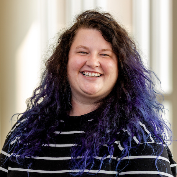 Headshot of Tetta, smiling and with brown and purple curly hair