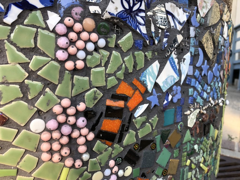 A close-up of a planter covered in multi-colored tile fragments and beads.